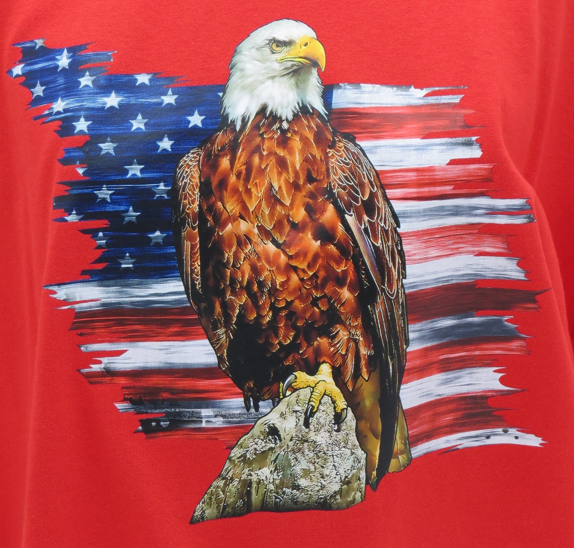 Our striking Red Eagle T-Shirt, a bold statement piece that embodies patriotism and style.  Crafted from premium cotton, this t-shirt combines comfort with a powerful design featuring a majestic eagle poised before a partial American flag backdrop.