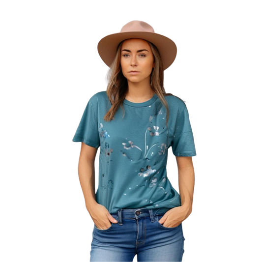Woman wearing a teal t-shirt with floral designs and a beige hat on a white background